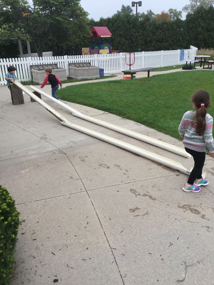 Children playing with long white pipes on a concrete path