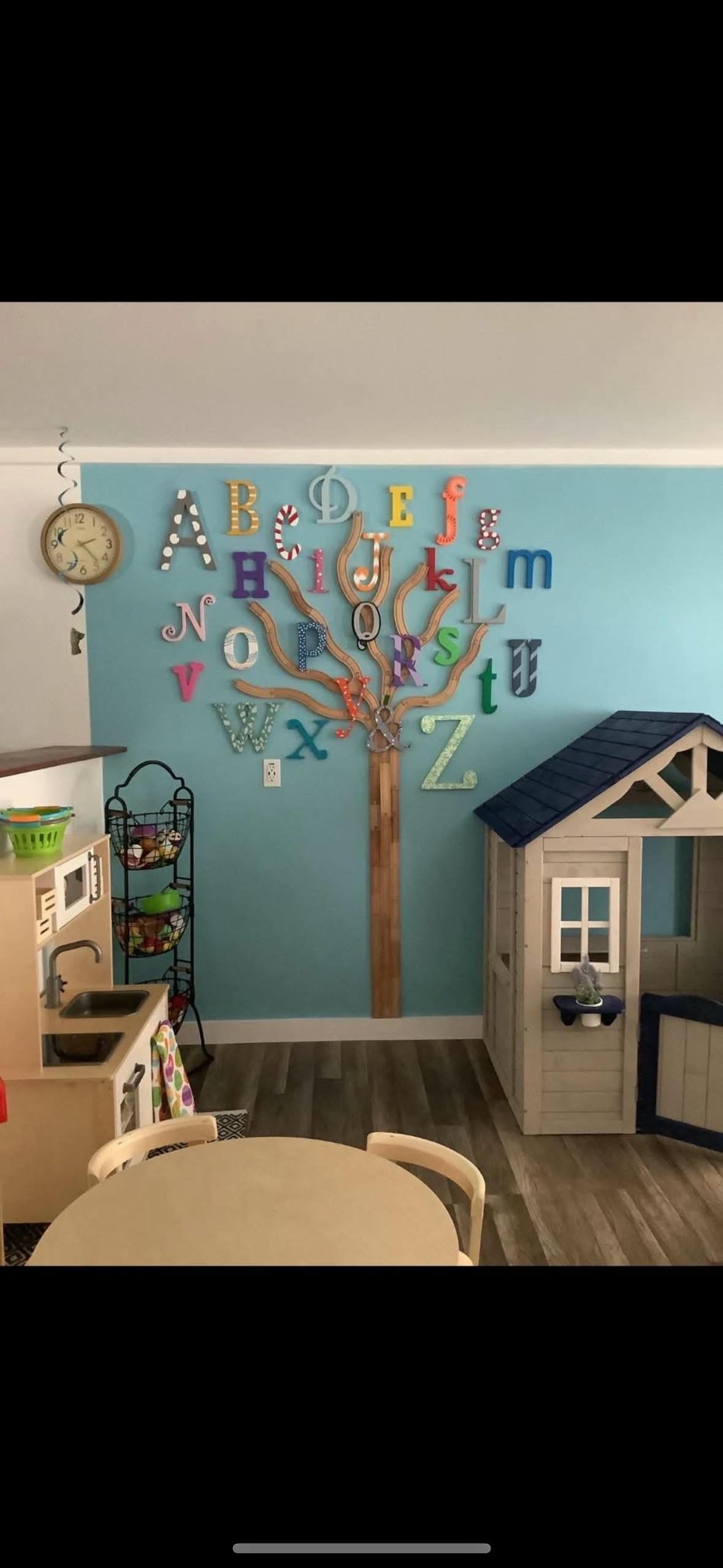 Playroom with alphabet tree on wall, play kitchen, and playhouse
