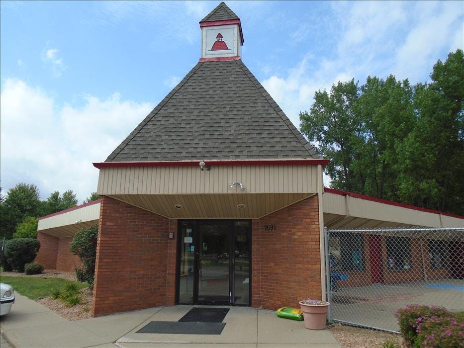 Brick building with a steep shingled roof and a cupola, a glass entrance