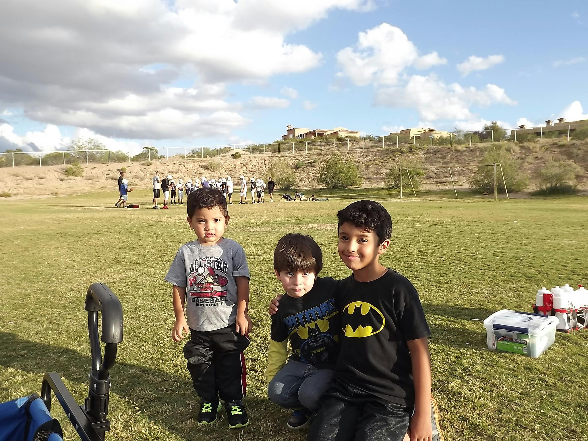 Three children on a grassy field with other people in the background