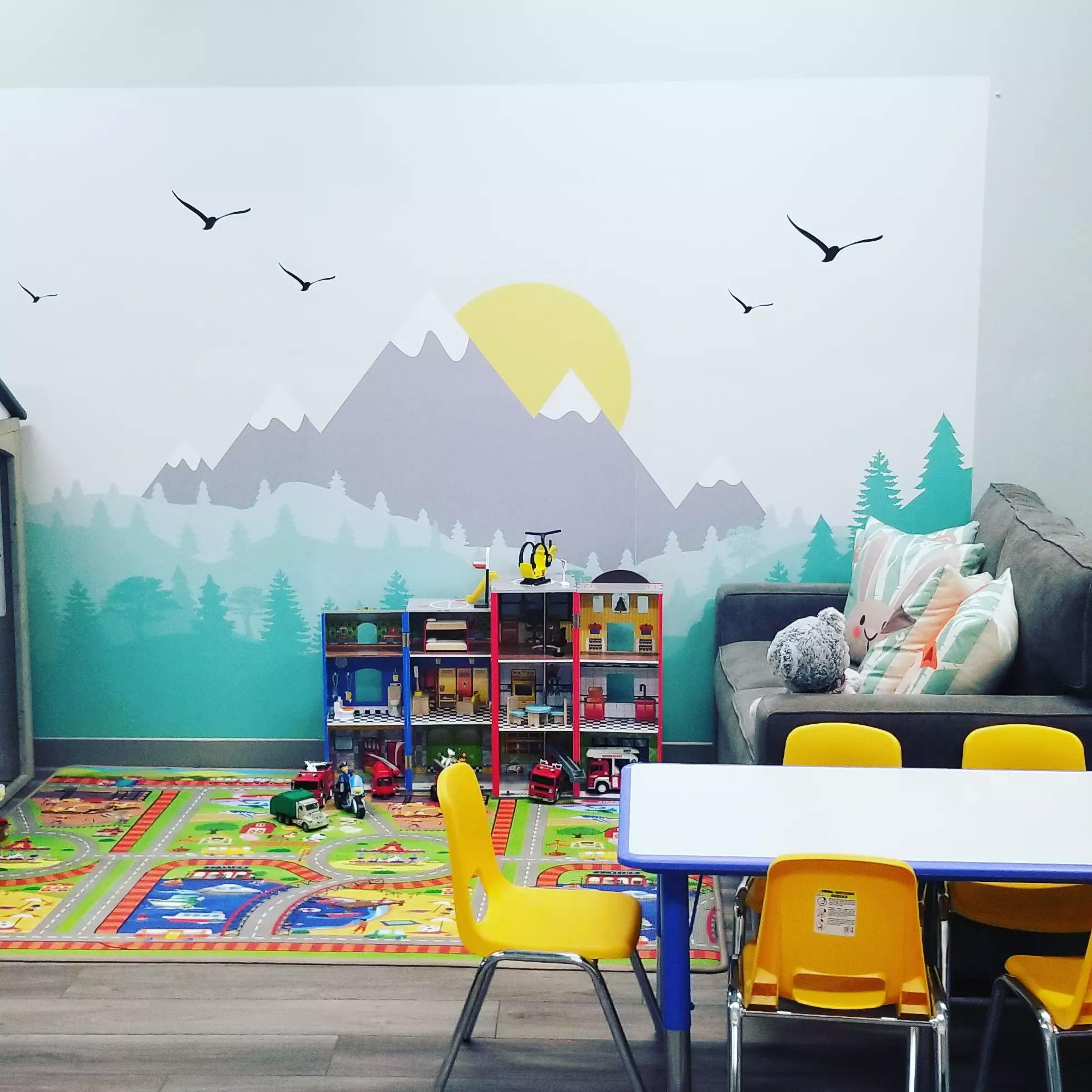 Playroom with a mountain mural, toy shelf, sofa, and child-sized table and chairs
