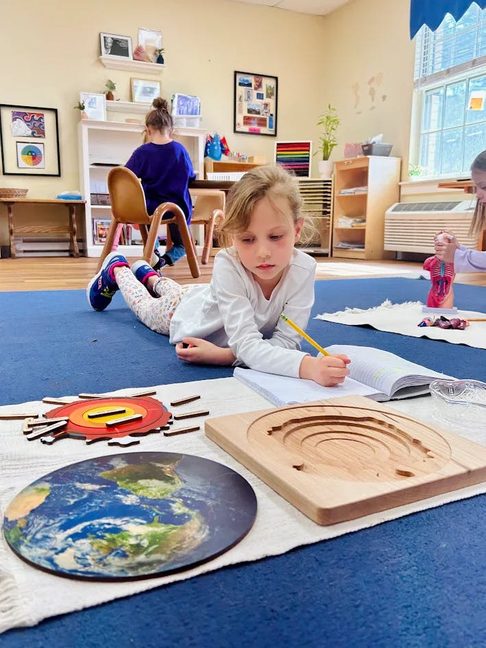 Child lying on the floor writing in a notebook next to earth science puzzles