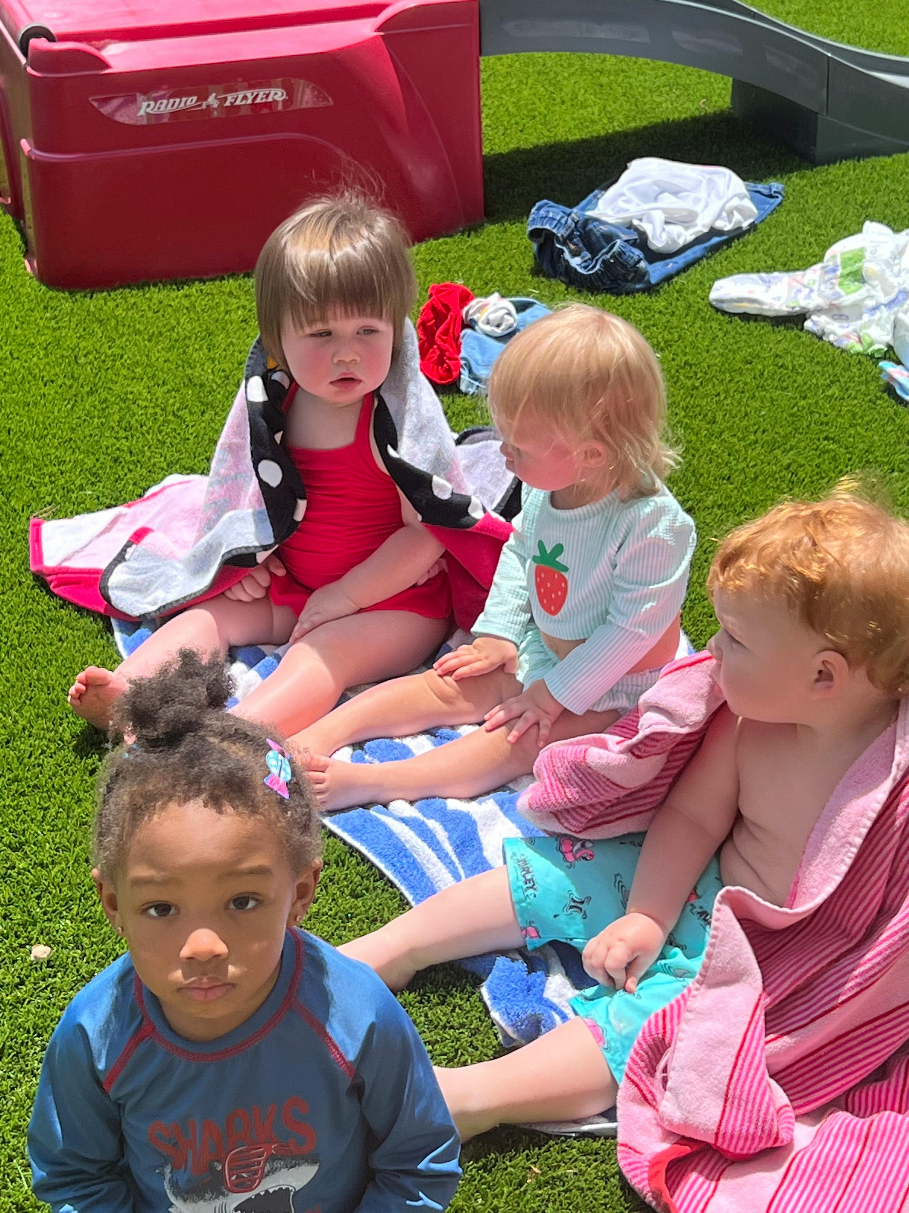 Four children sitting on towels on green turf