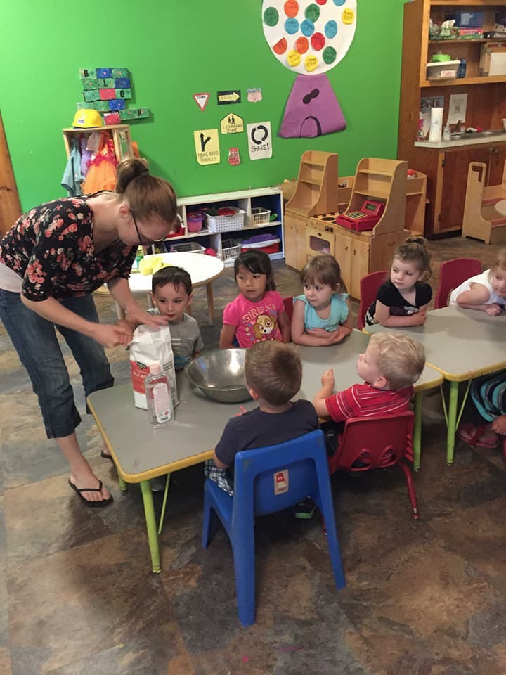 Adult and children at a table with a bag of flour and a bowl