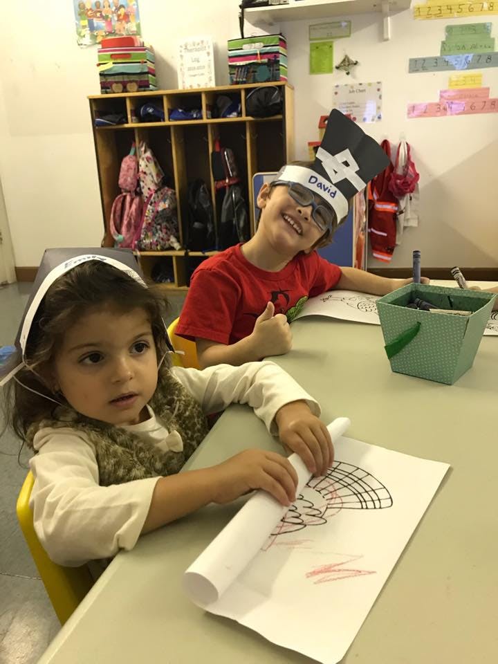Two children at a table, one drawing and one smiling