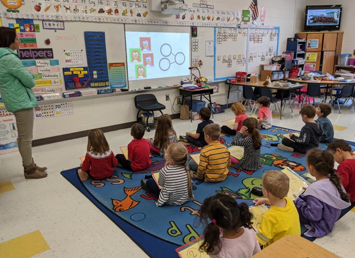 Adult standing in front of children sitting on a rug in a classroom
