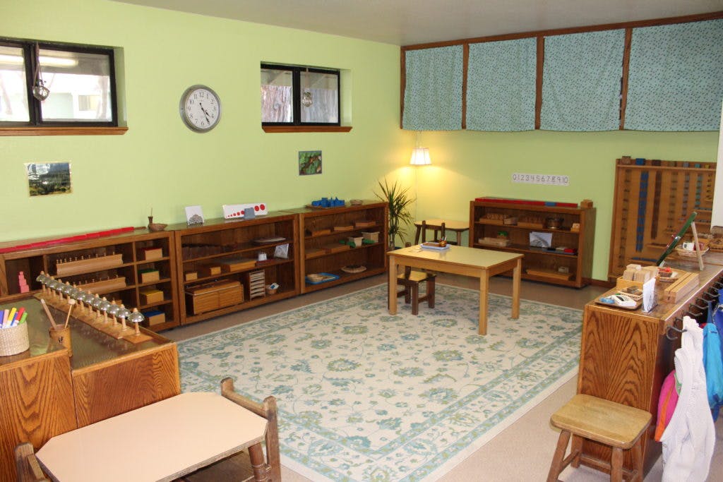 Classroom with wooden shelves, tables, and a patterned rug