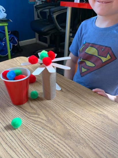 Child in a blue shirt with a red cup and craft items on a wooden table