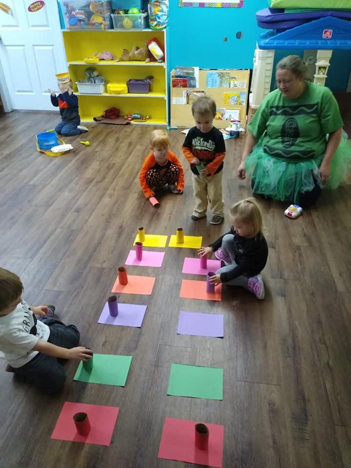 Adult and children playing with colored paper and cardboard tubes on the floor