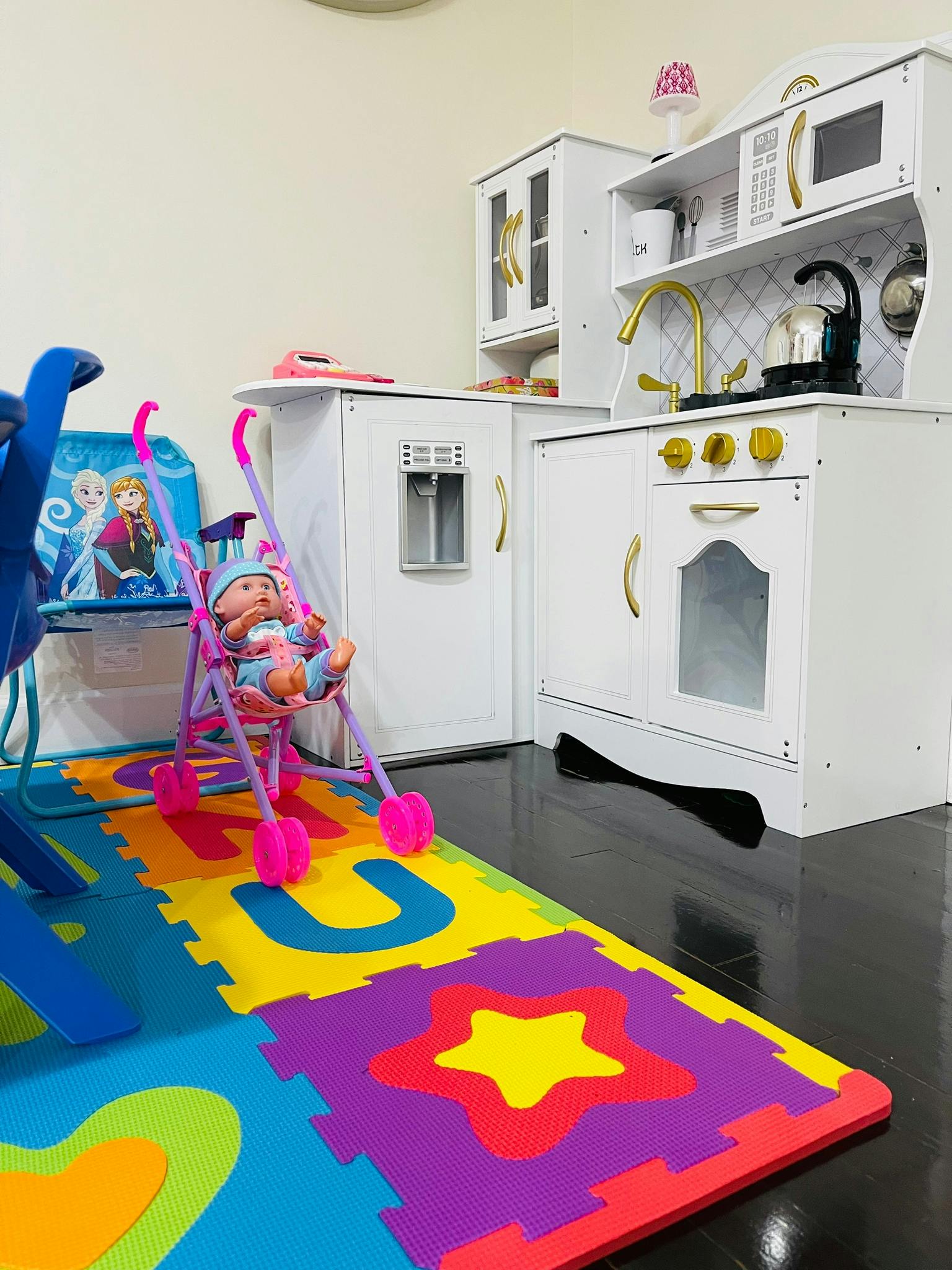Doll in a stroller on a colorful playmat in a play kitchen