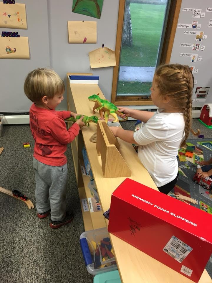 Two children playing with dinosaur toys on a ramp in a classroom