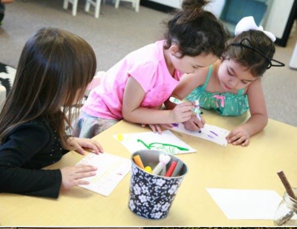 Three children drawing at a table in a classroom