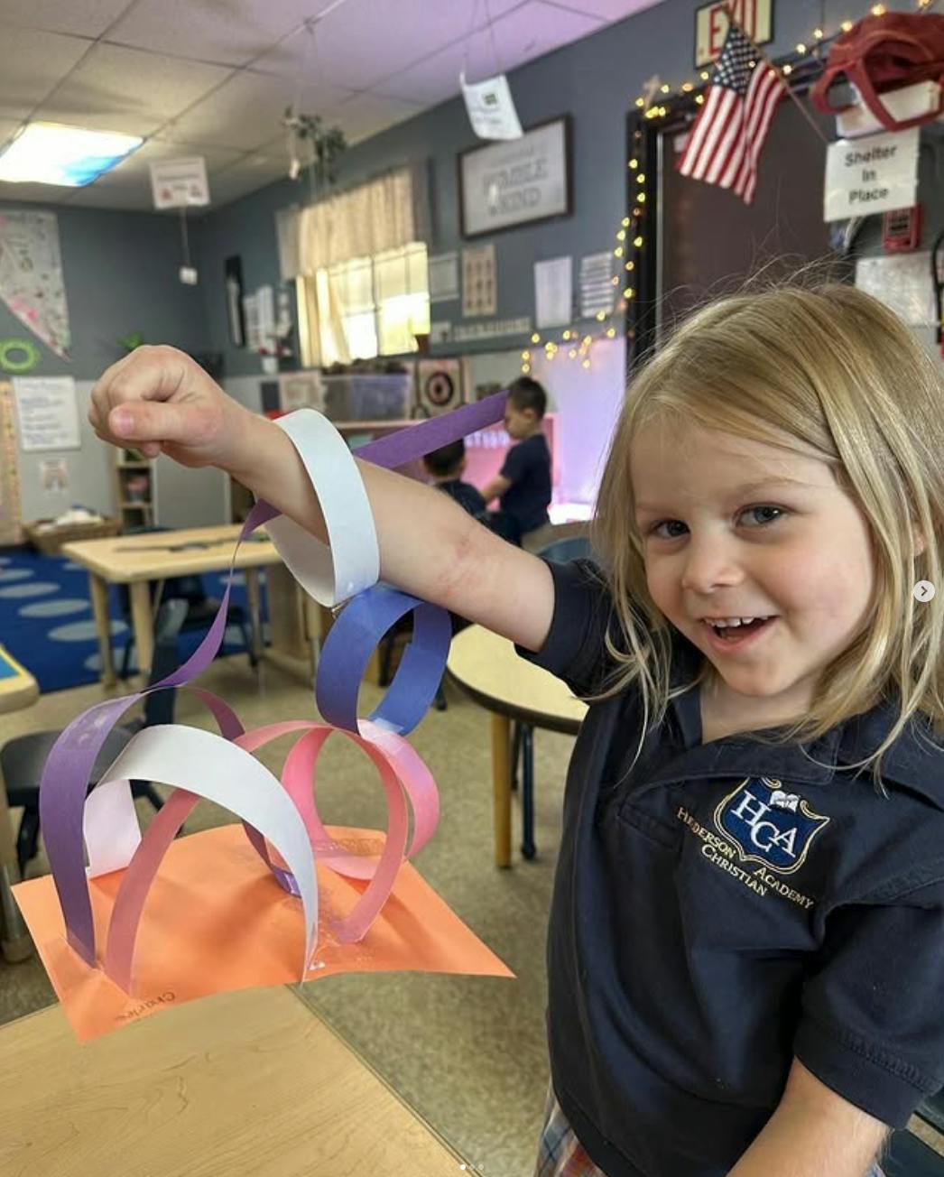 Child in a classroom holding up a colorful paper chain craft