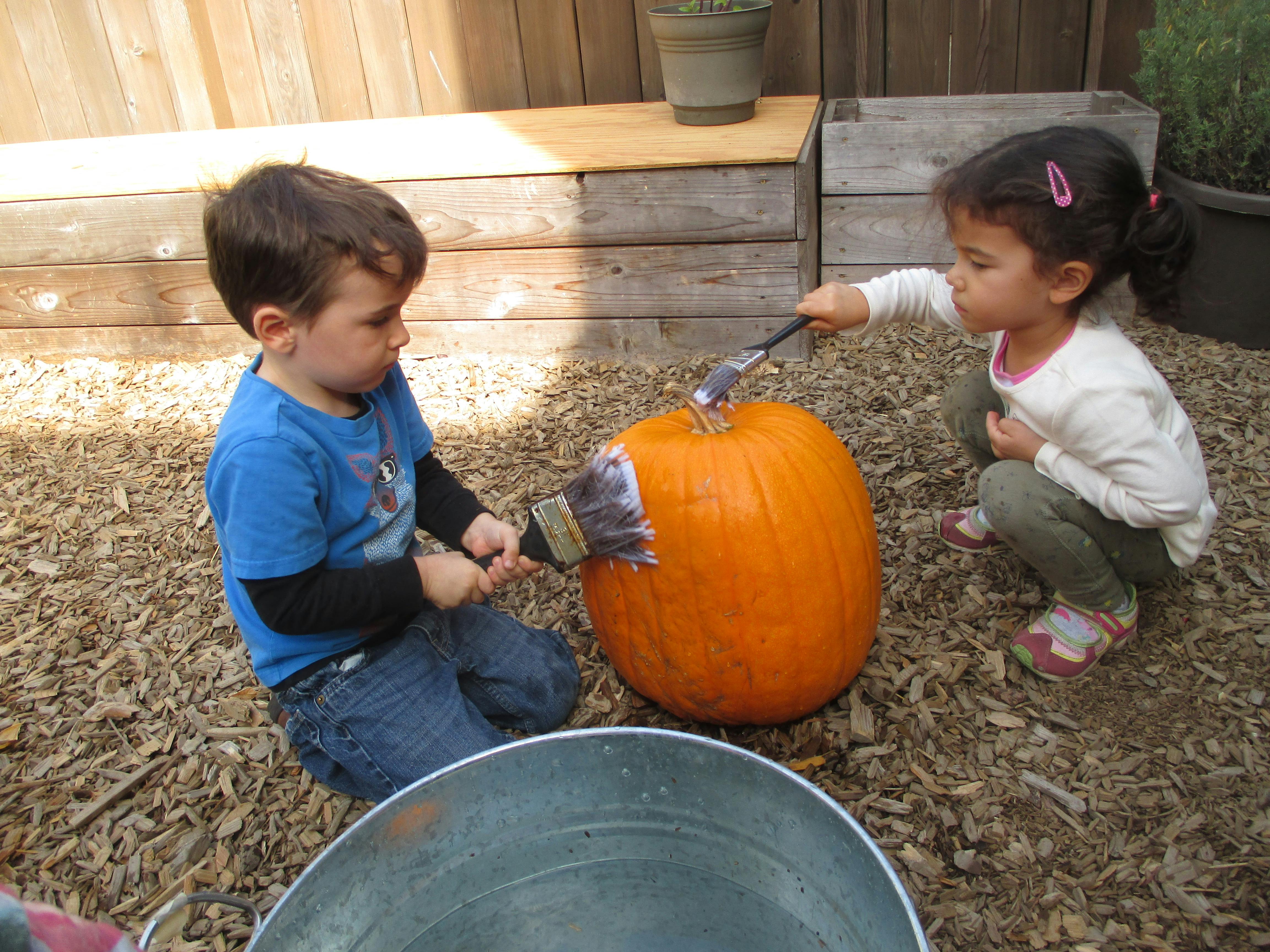 Two children painting a pumpkin outdoors