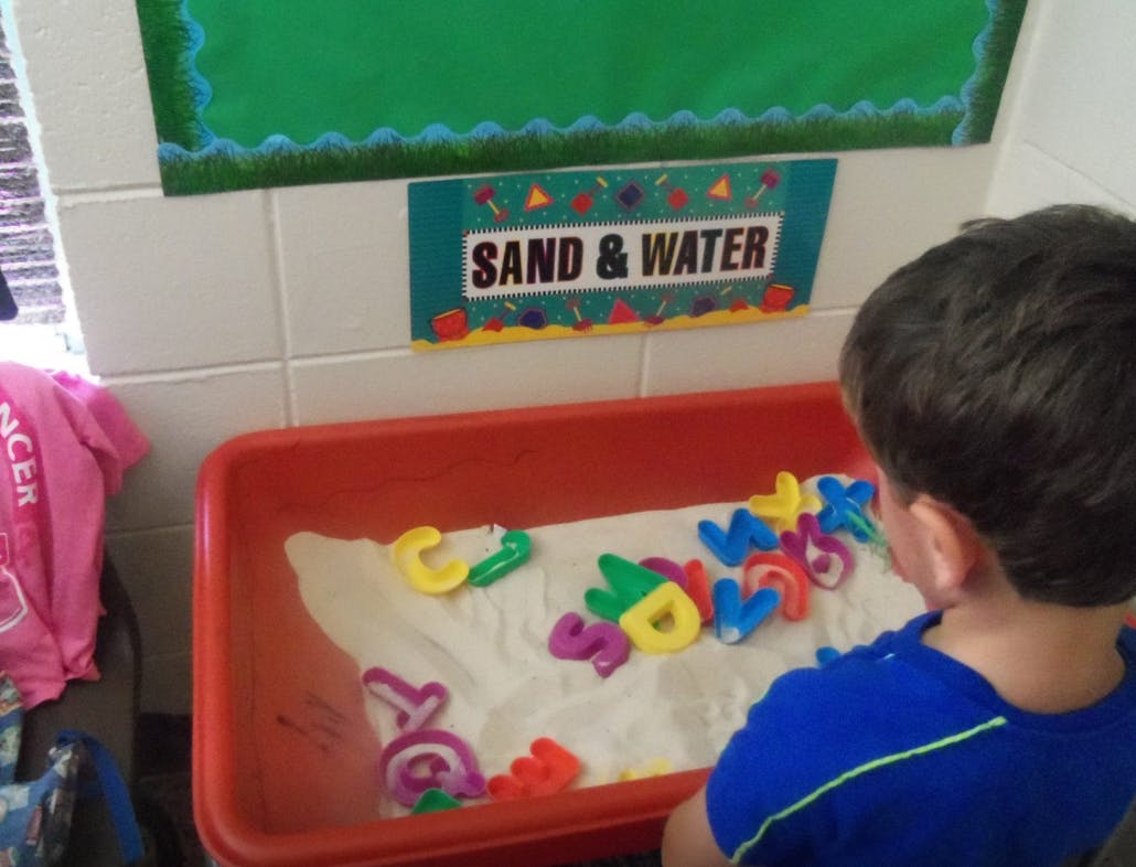 Child looking at colorful letters in a sand and water table