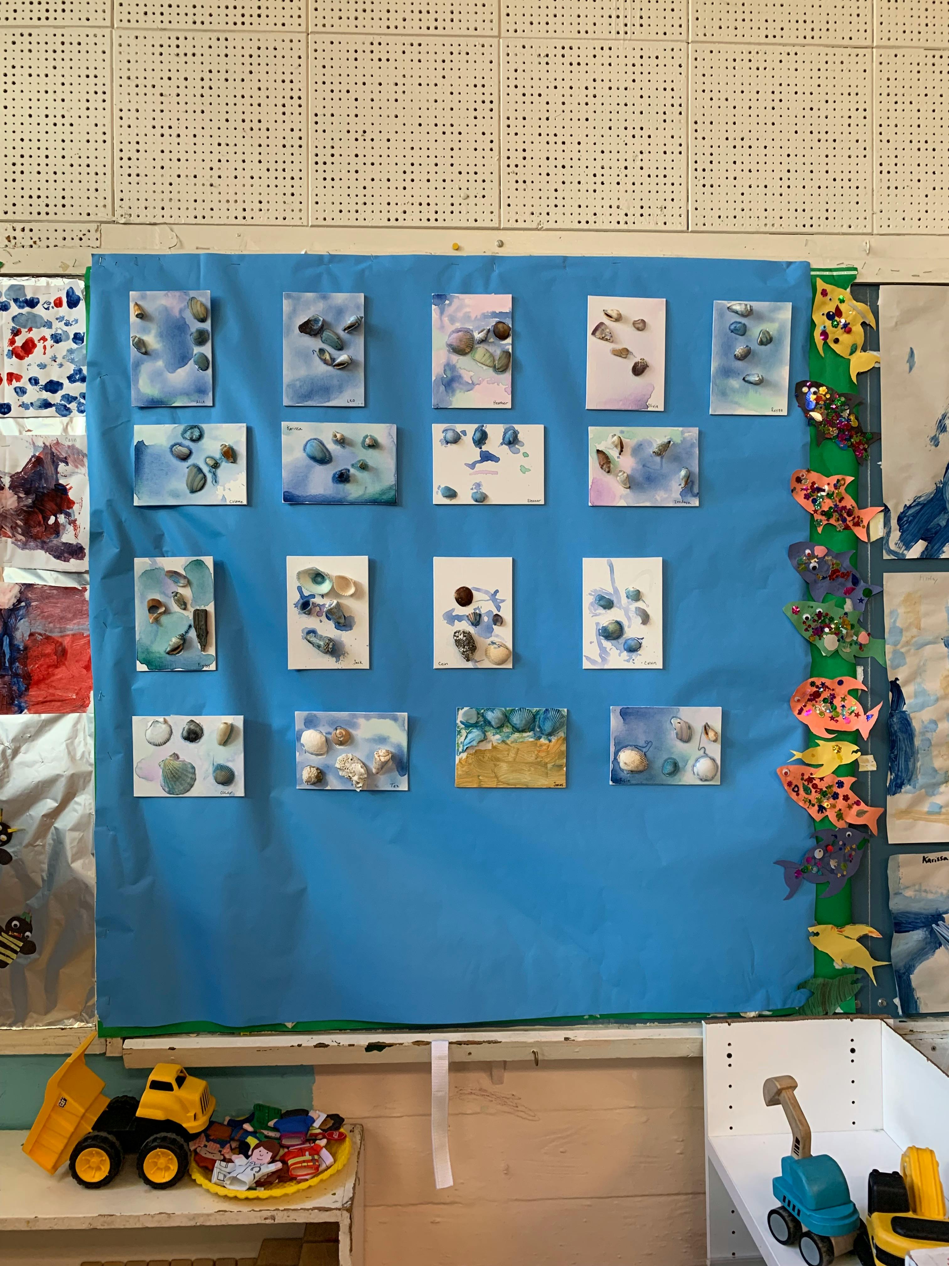 Children's artwork of shells and pebbles on blue paper
