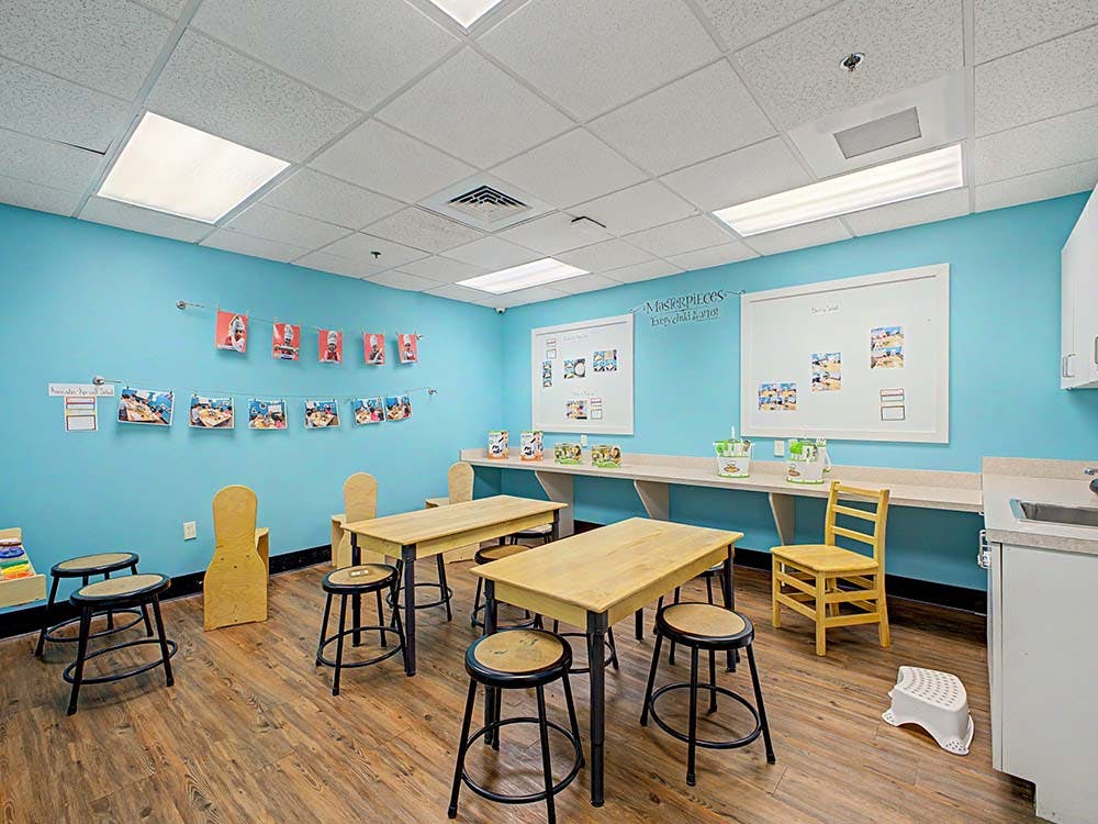 Classroom with blue walls, wooden tables, stools, and children's artwork displayed