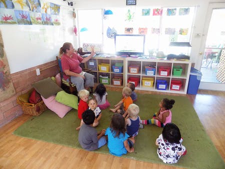 Adult reading to a group of children sitting on a rug in a classroom
