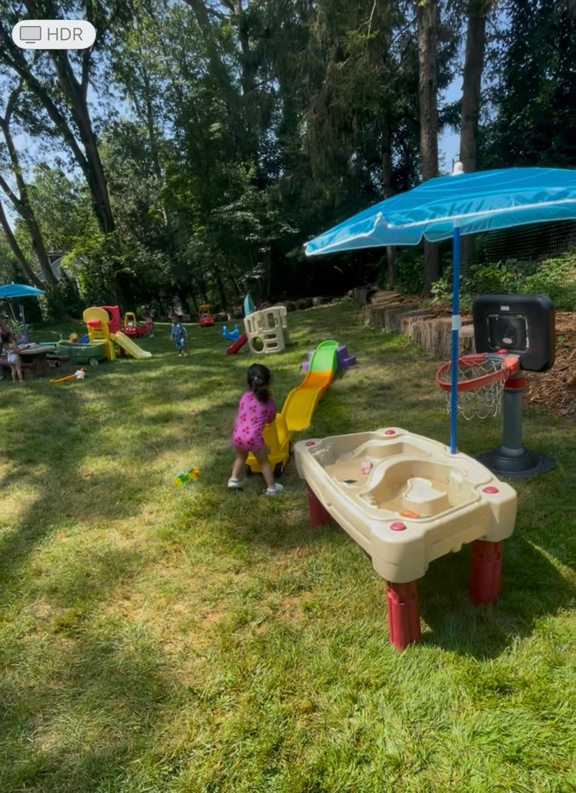 Child playing with a yellow slide and toy truck in a grassy yard