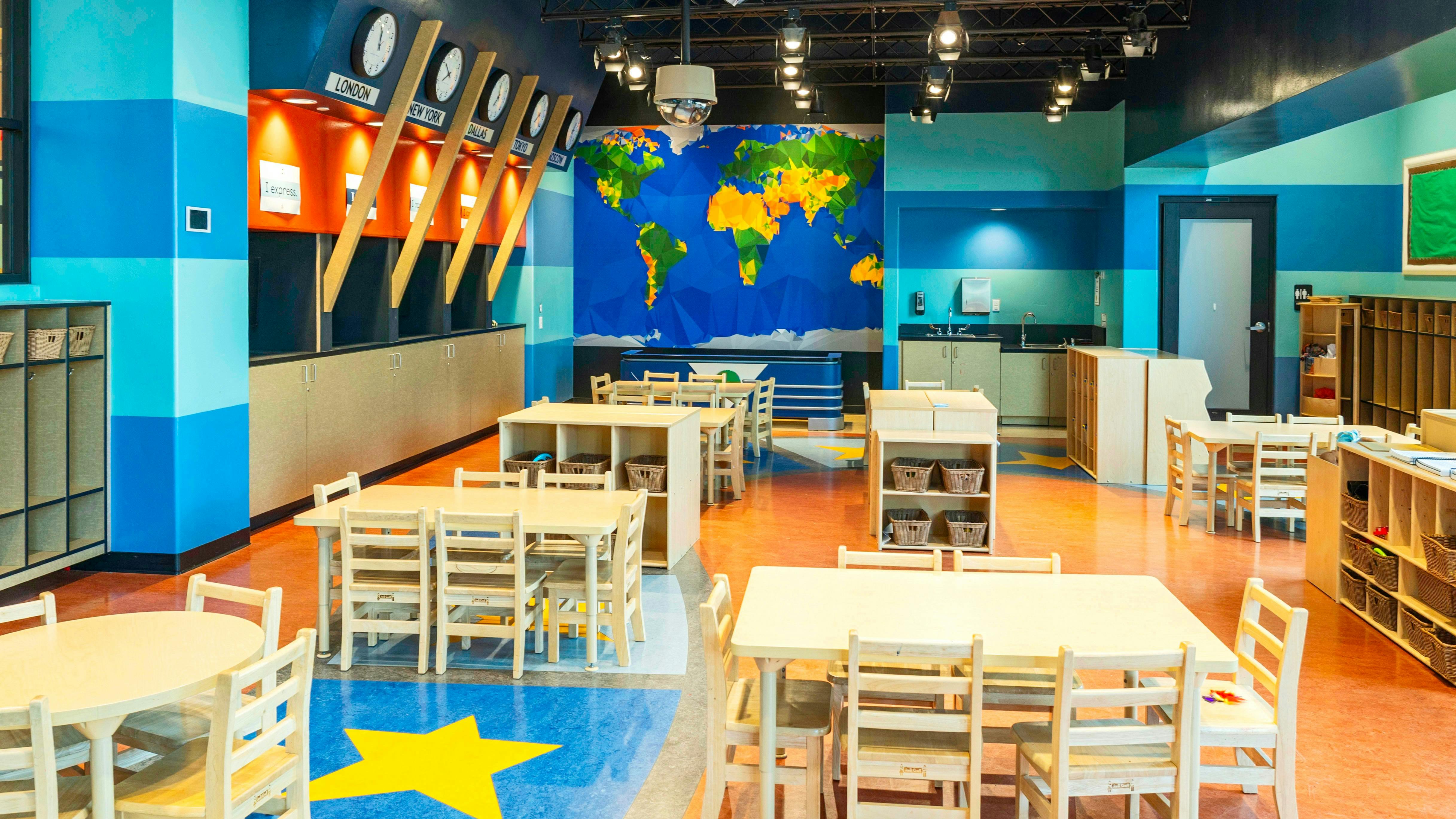 Children's classroom with small tables and chairs, world map mural, and clocks