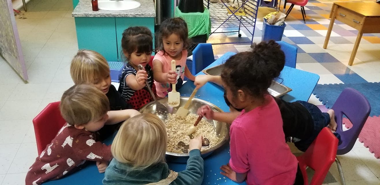 Children gathered around a table mixing ingredients in a large bowl