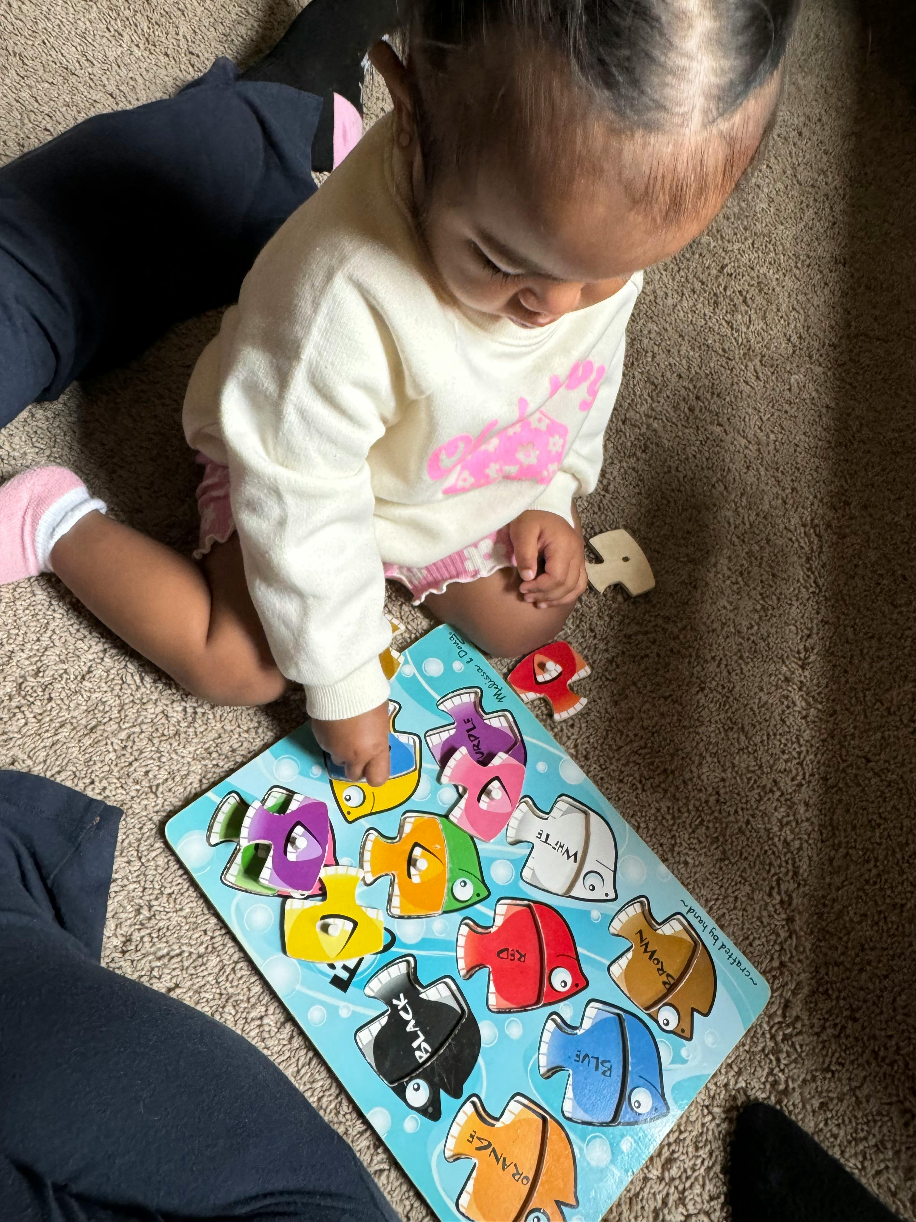 Child playing with a colorful fish puzzle on the floor