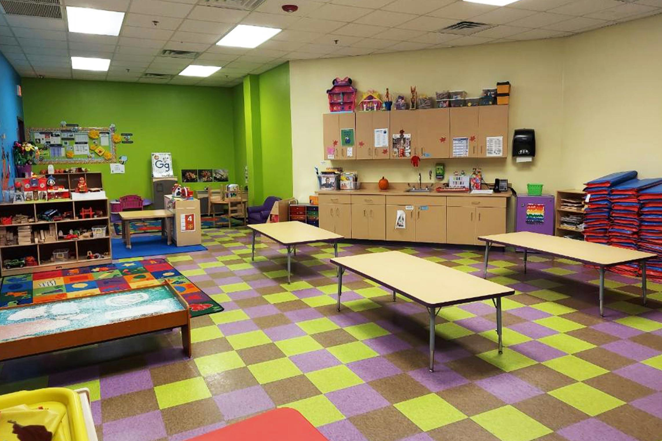 Empty classroom with green and beige walls, tables, and toys