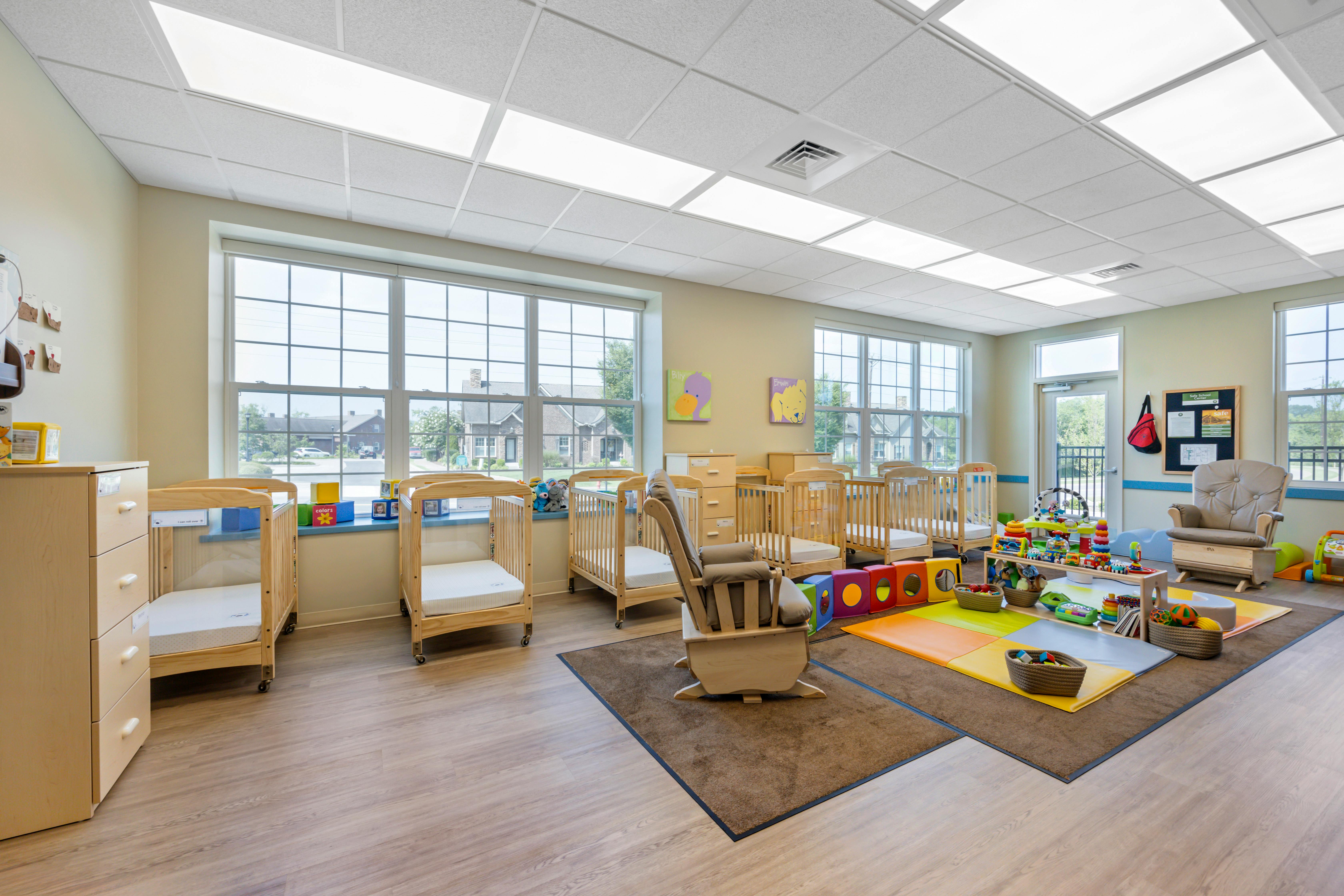 A brightly lit nursery with multiple cribs, a rocking chair, and play mats
