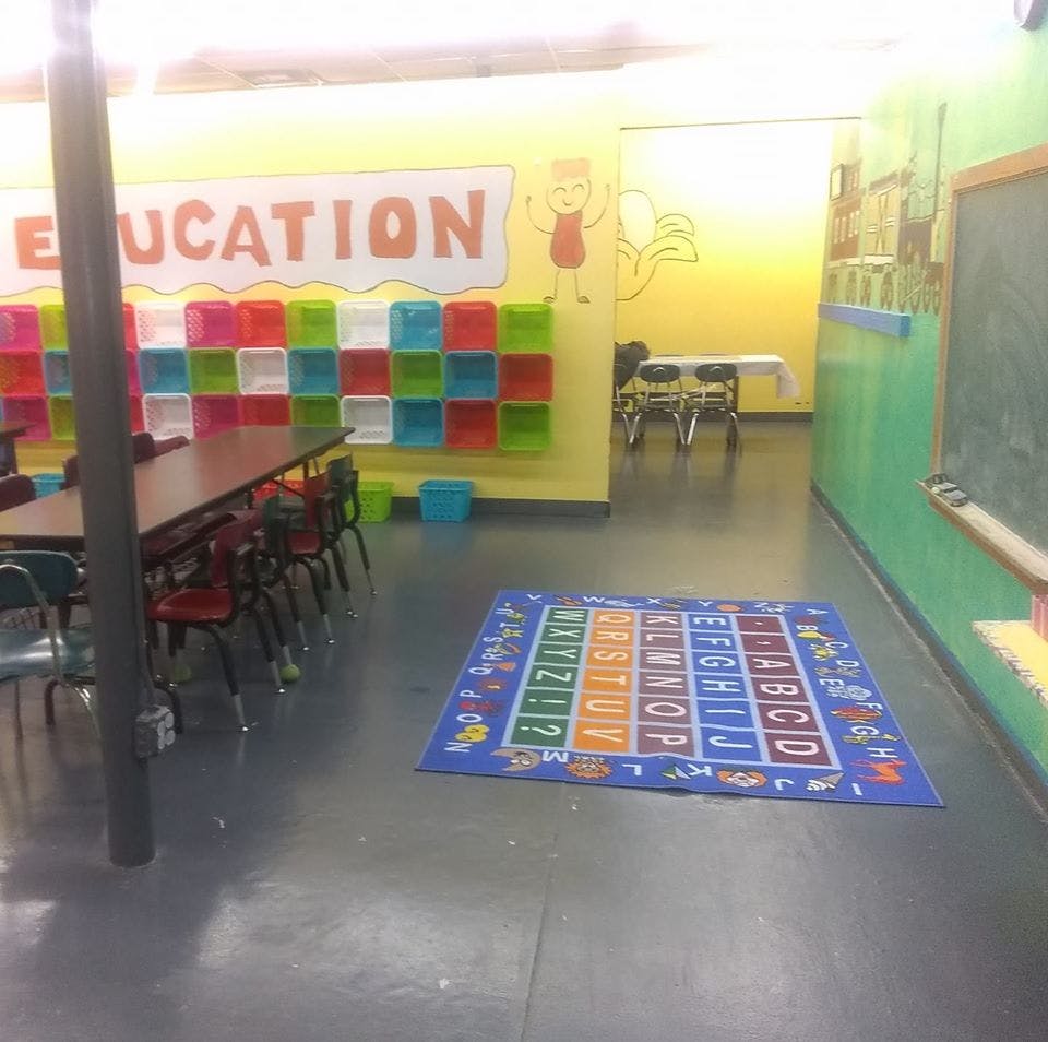 Classroom with tables, chairs, colorful storage, and an alphabet rug