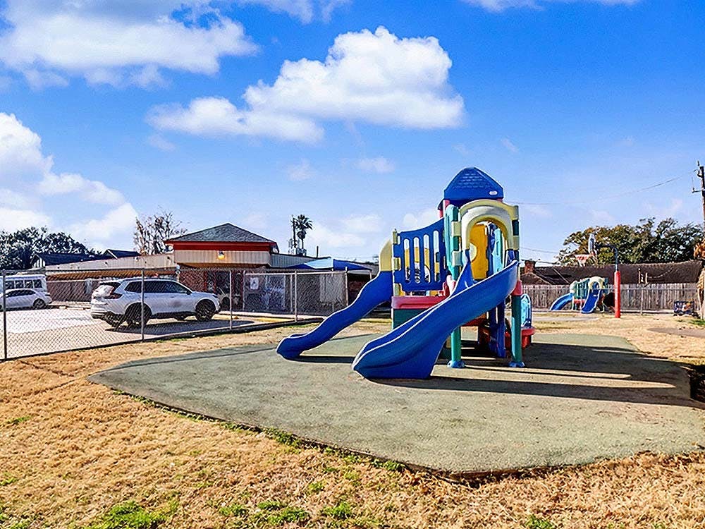 Colorful playground structure with slides on a mat, surrounded by dry grass
