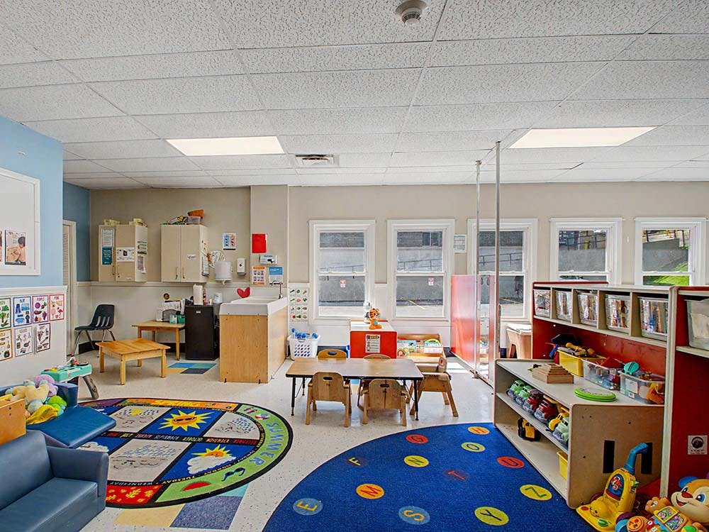 A colorful children's classroom with small tables, chairs, and play mats