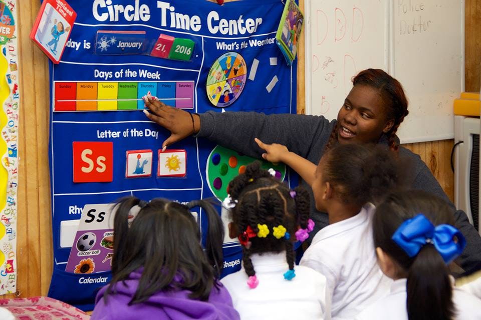 Person pointing to a "Circle Time Center" chart with children watching