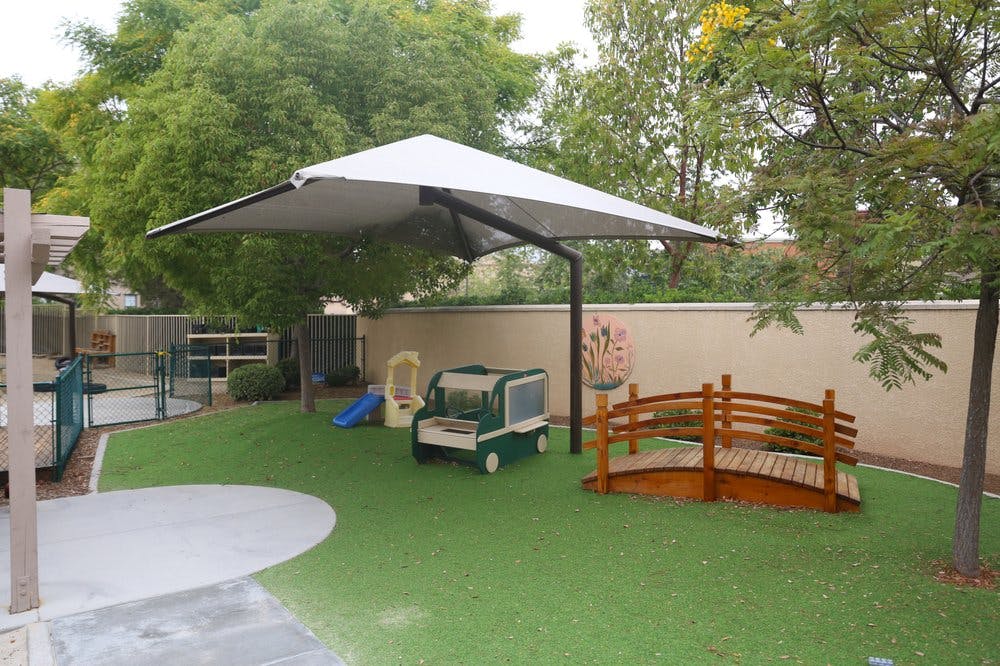 Outdoor play area with artificial turf, shade structure, and play equipment
