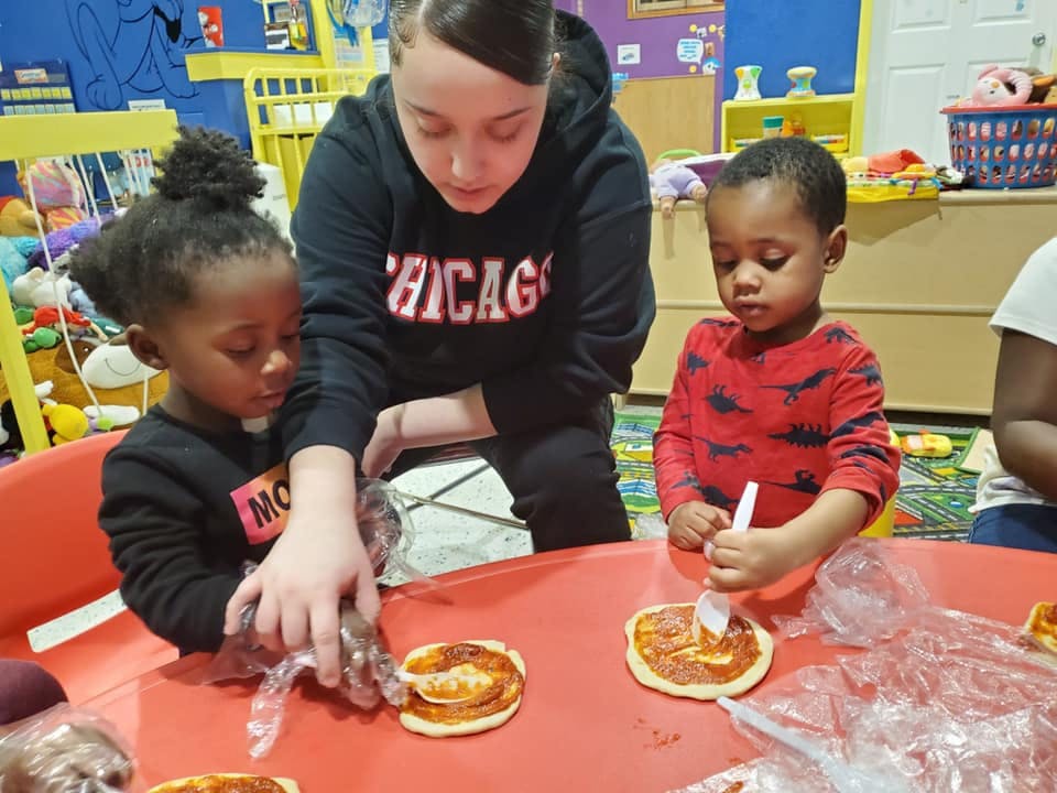 Person helping two children make mini pizzas at a table