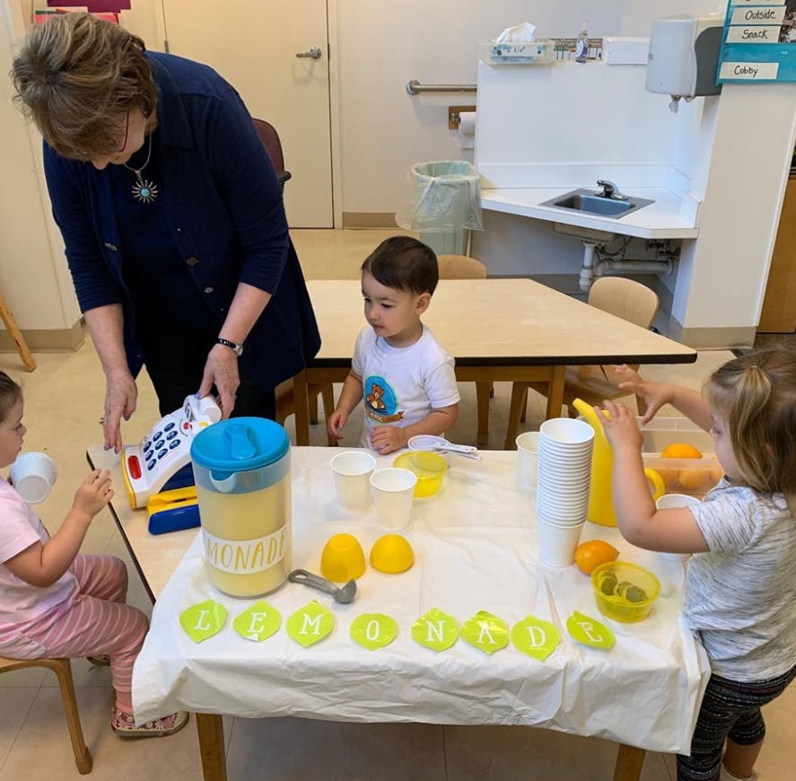Adult and three children playing with a toy cash register and lemonade stand