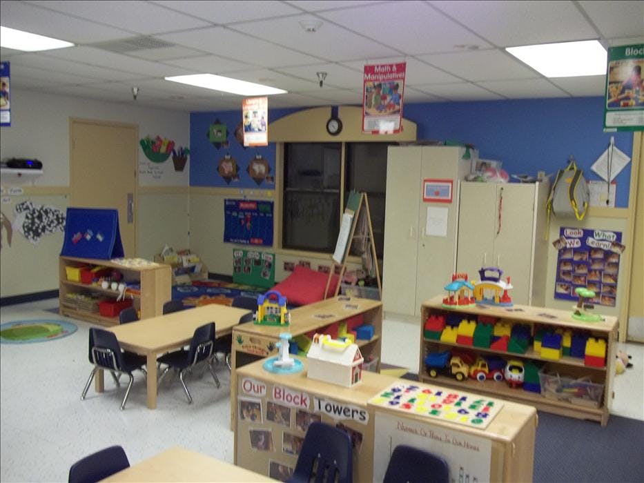 Classroom with tables and chairs, shelves of toys and blocks, and wall decorations