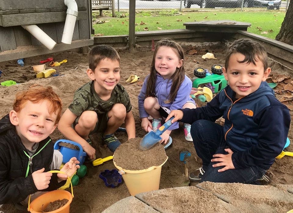Four children playing in a sandbox with buckets and shovels