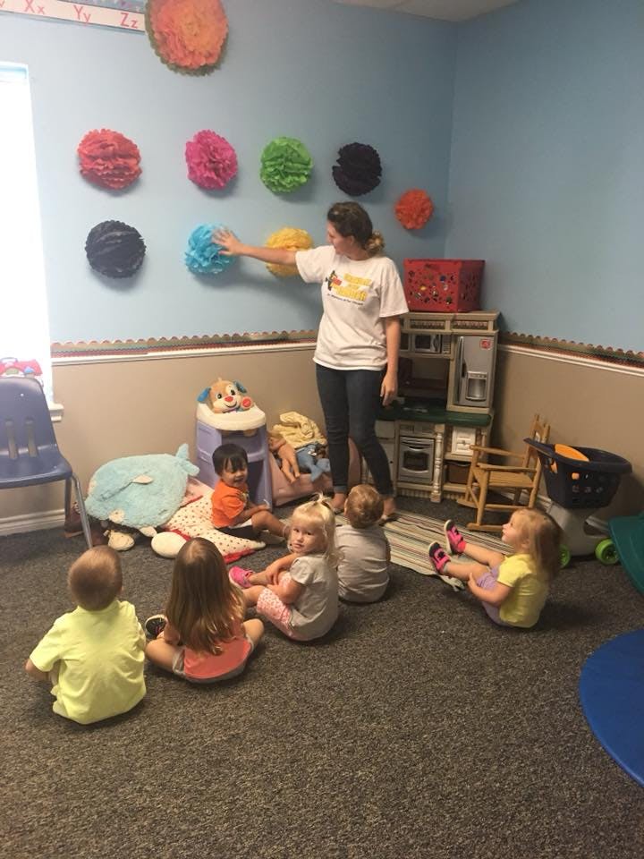 Person standing in a classroom with several children sitting on the floor