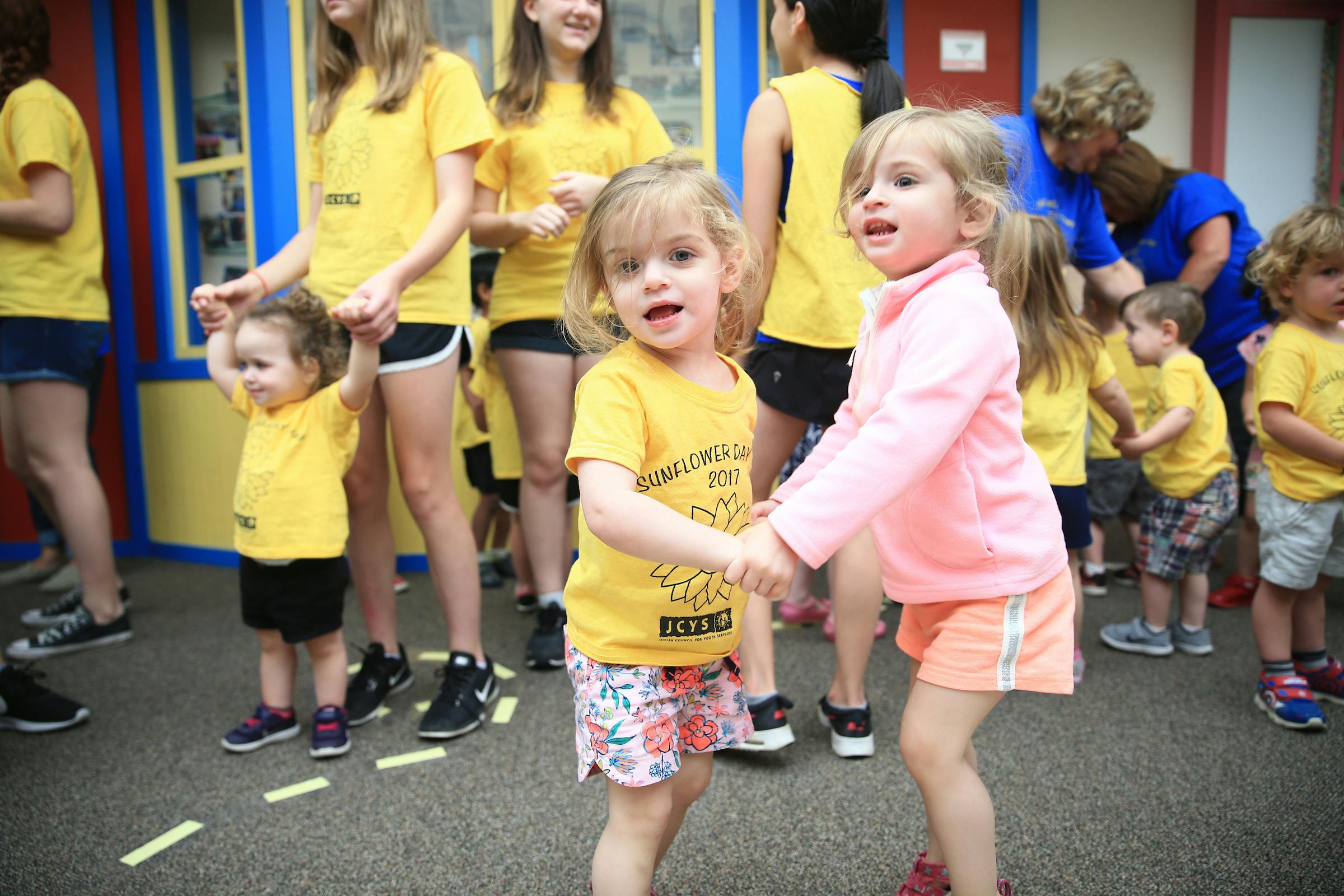 Two children holding hands and dancing, with other people in the background