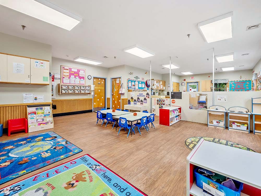 Colorful classroom with small tables and chairs, play mats, and learning materials