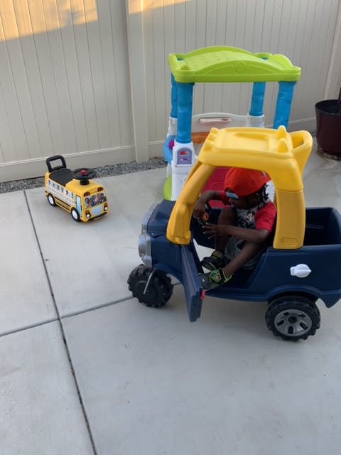 Child in a toy car next to a toy bus and play structure