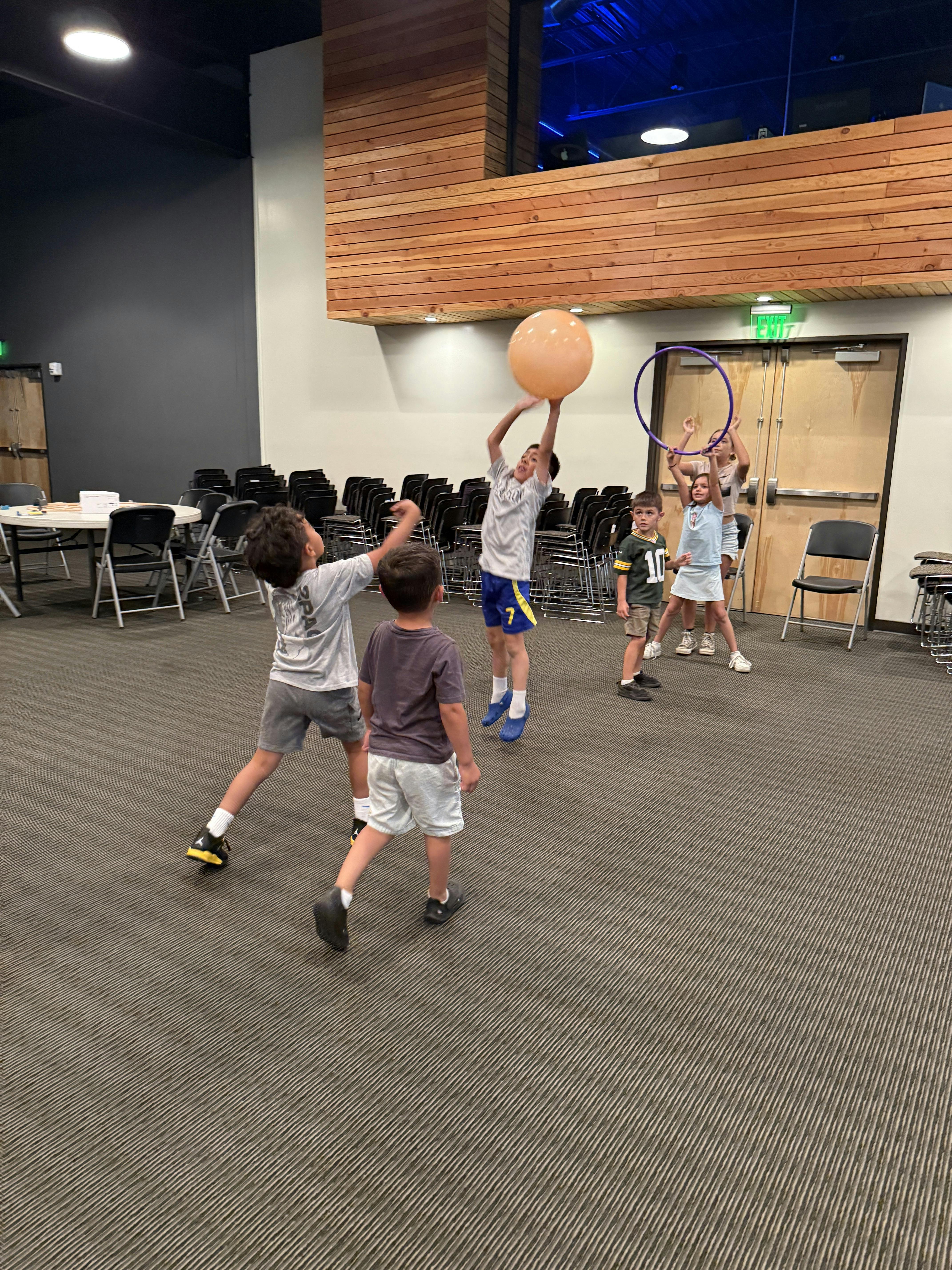 Group of children playing with a large ball and a hula hoop in a room