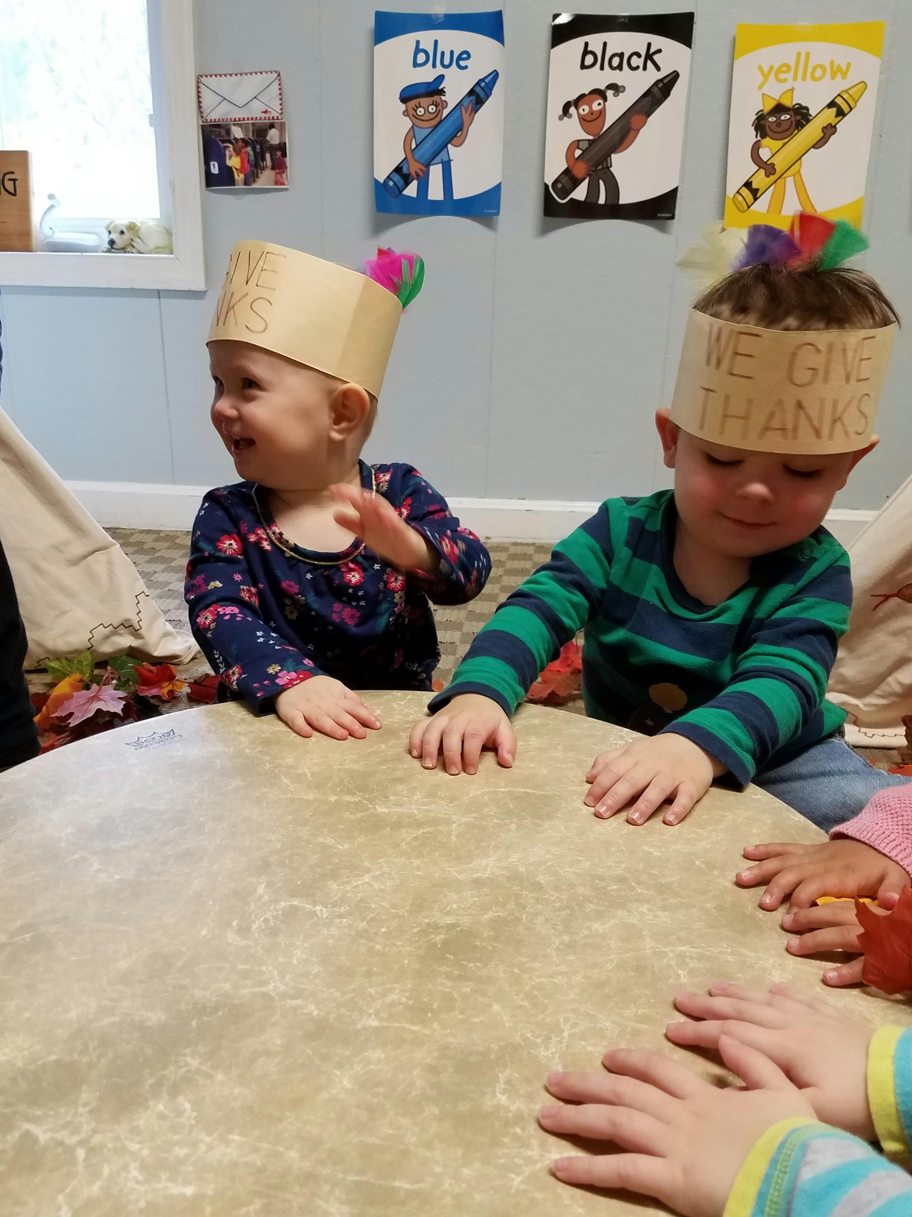 Two children wearing paper crowns playing around a large drum