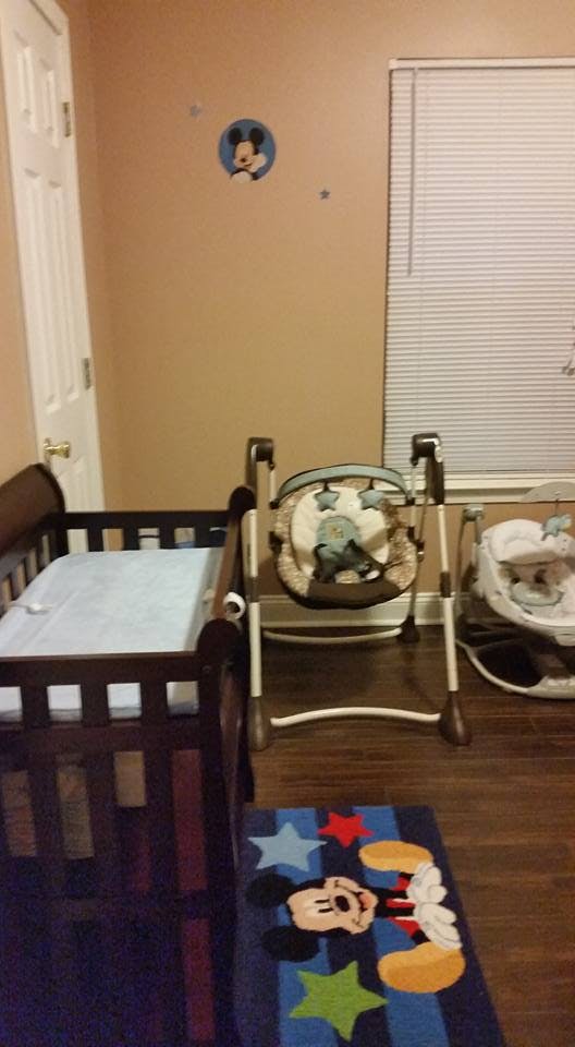 Baby crib, swing, and bouncer in a room with a Mickey Mouse rug