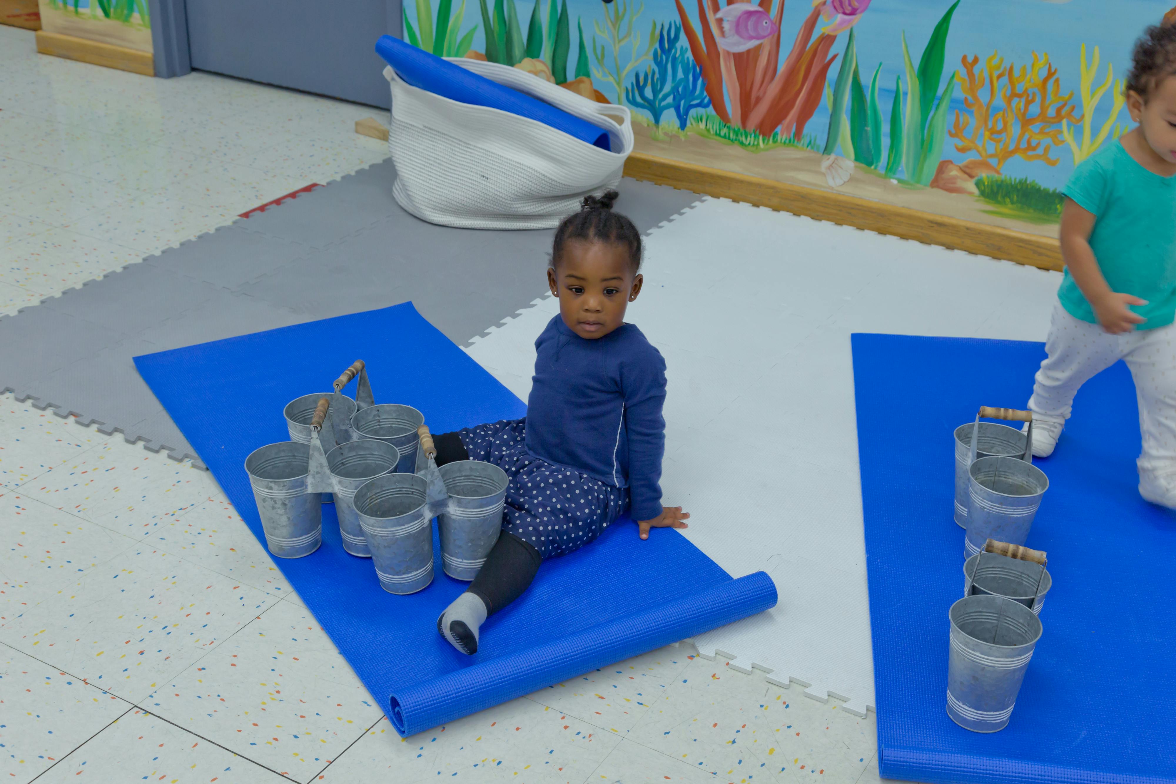 Child sitting on a blue mat with buckets