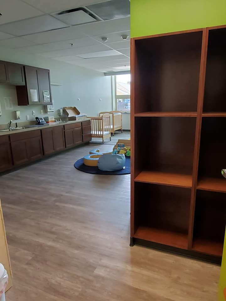 Empty classroom with cribs, cabinets, and a bookshelf
