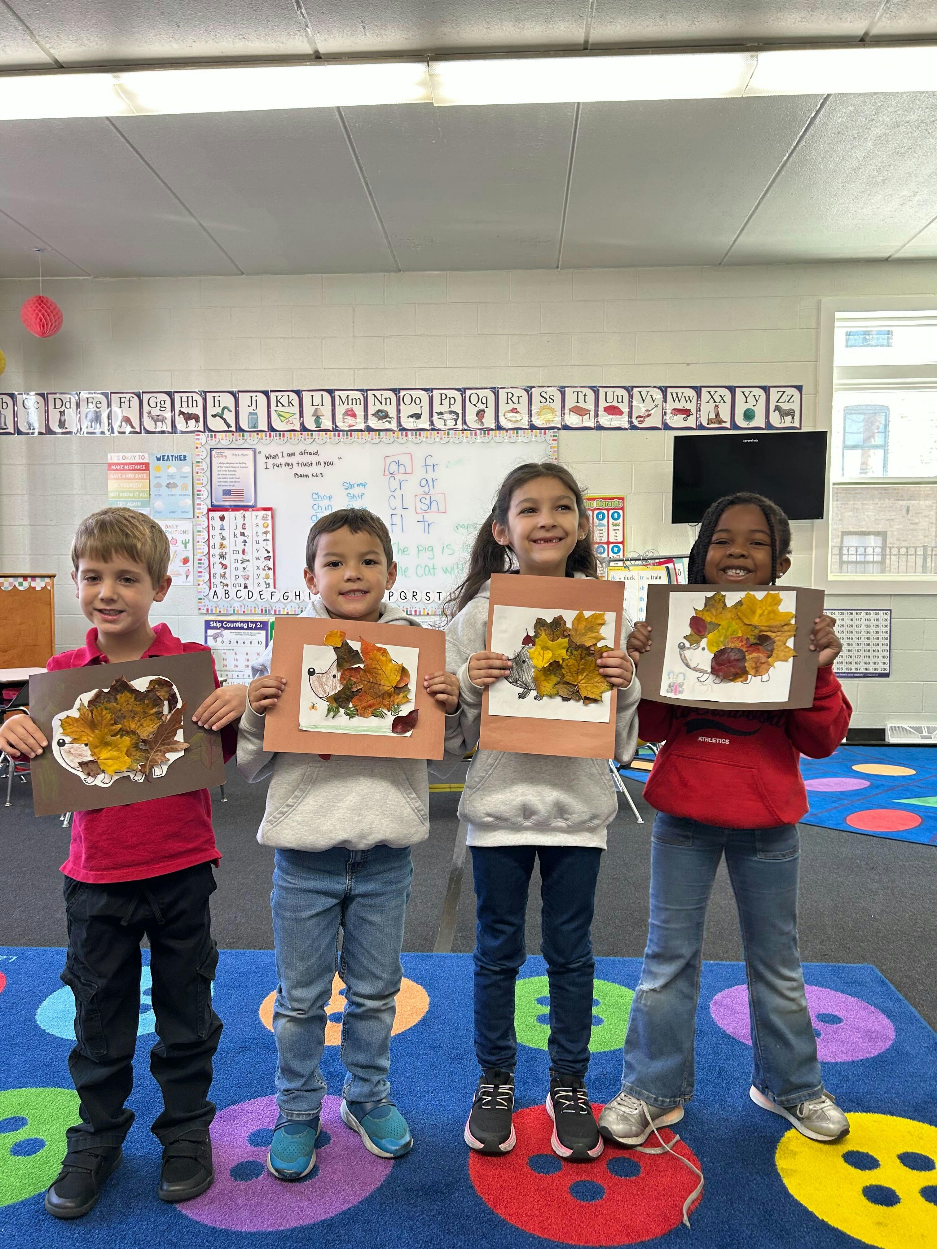 Four children holding up leaf collages in a classroom