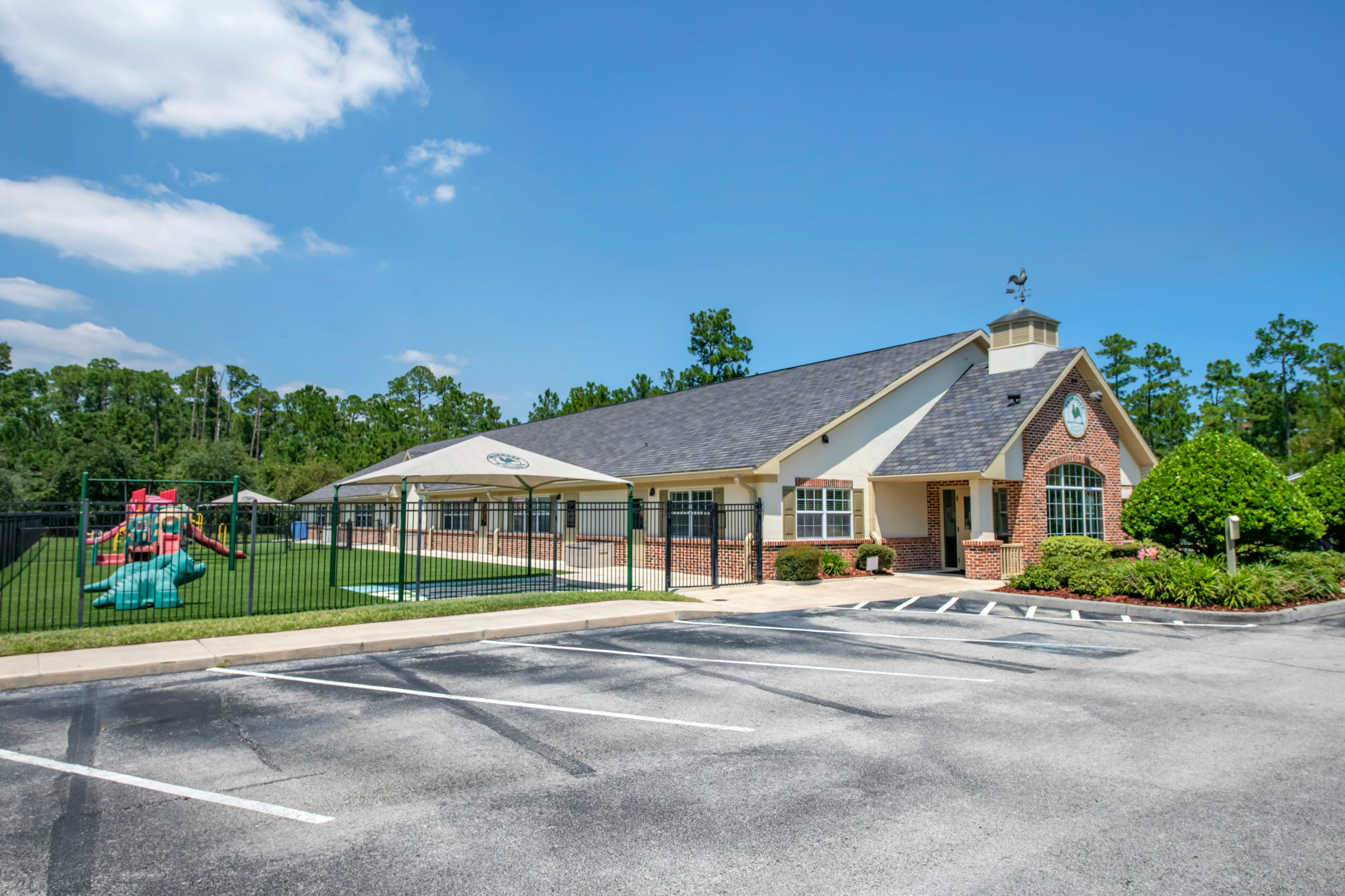Exterior of a daycare or school building with a fenced playground and parking lot