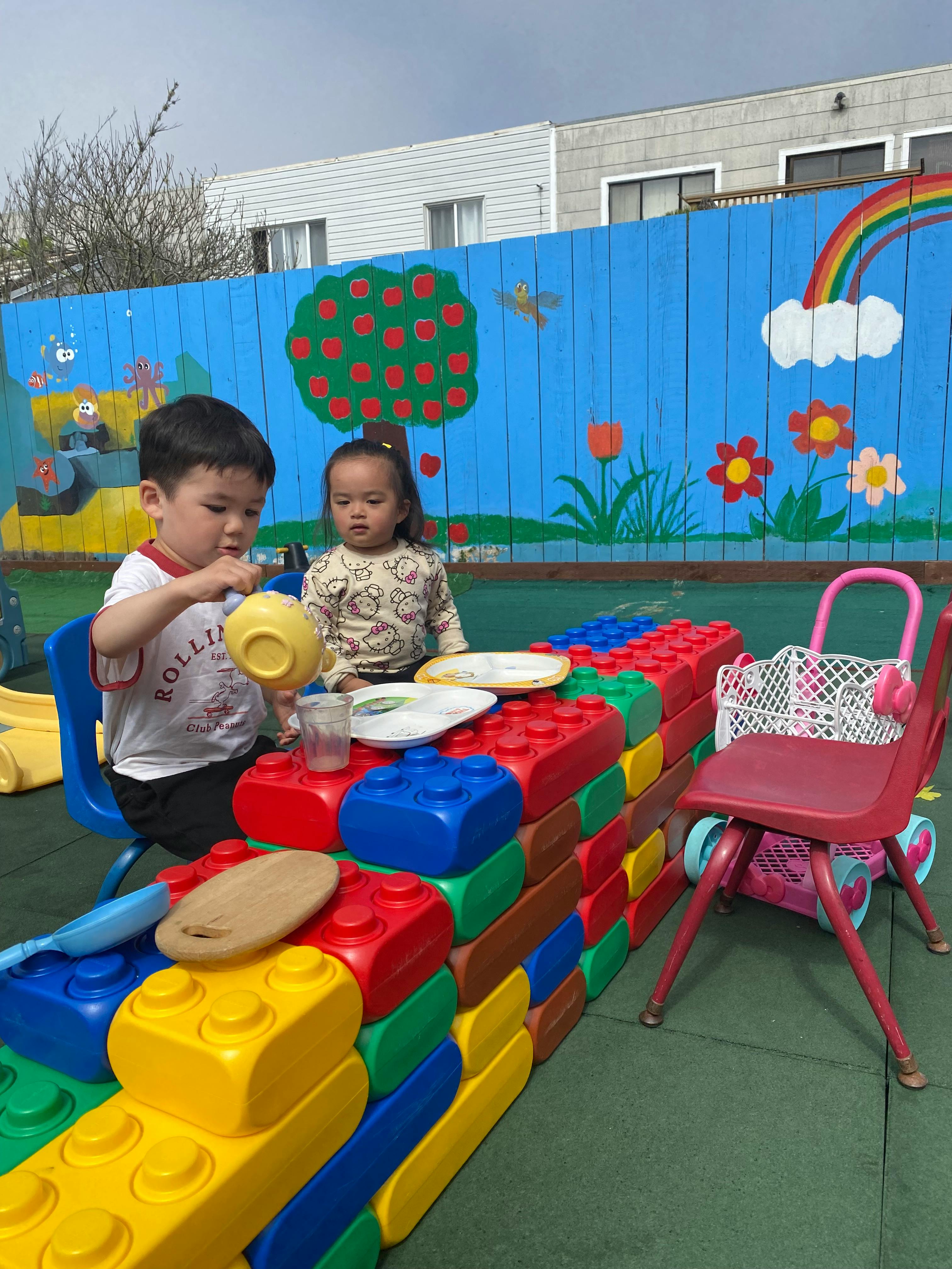 Two children playing with toy dishes at a block table outdoors