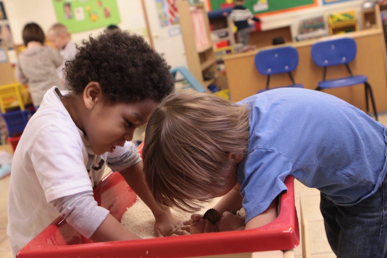 Two children playing in a red sand table in a classroom